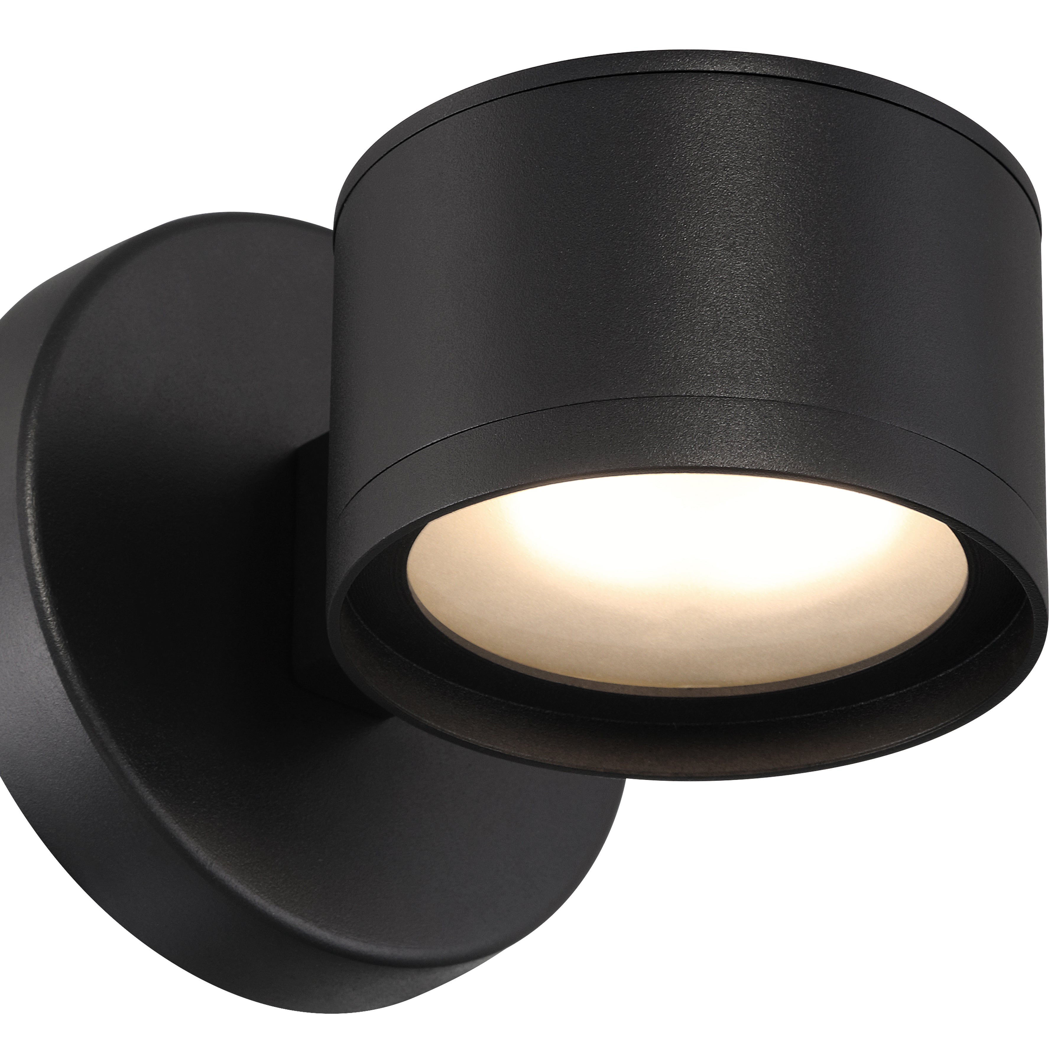The Ari Bare Outdoor LED Wall Mount by Access Lighting is a modern black wall-mounted fixture featuring a round base and cylindrical shade, illuminated and angled slightly downward.