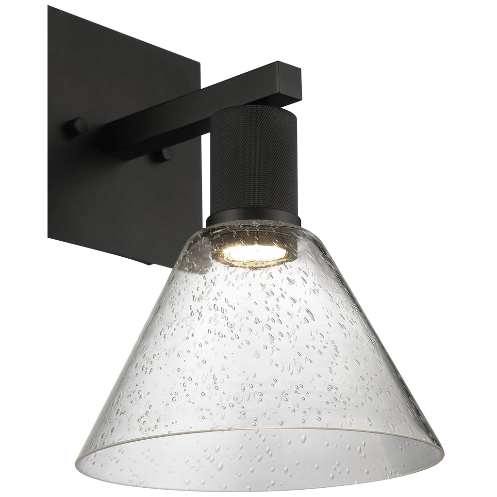 The Port Nine Martini LED Wall Sconce by Access Lighting features a matte black metal base and a clear, cone-shaped seeded glass shade with bubble details.