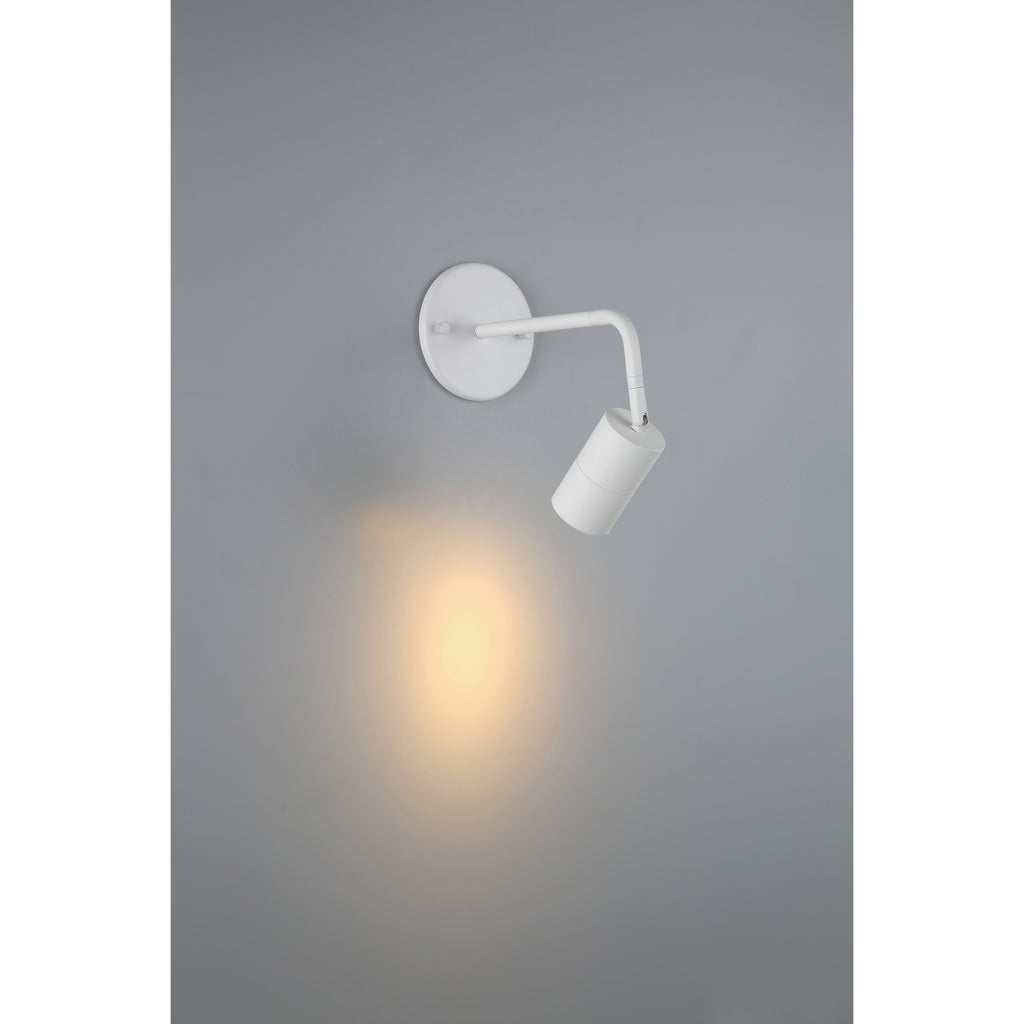 The Cafe Dual Mount 1 Light LED Wall or Ceiling Spotlight by Access Lighting in matte white is turned on, casting a soft yellow light onto a gray wall.