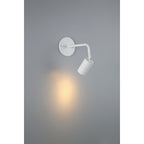The Cafe Dual Mount 1 Light LED Wall or Ceiling Spotlight by Access Lighting in matte white is turned on, casting a soft yellow light onto a gray wall.